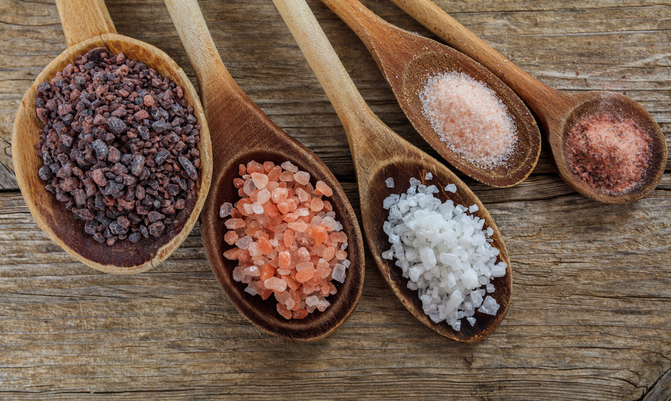 Variety of salts and peppercorns on wooden board